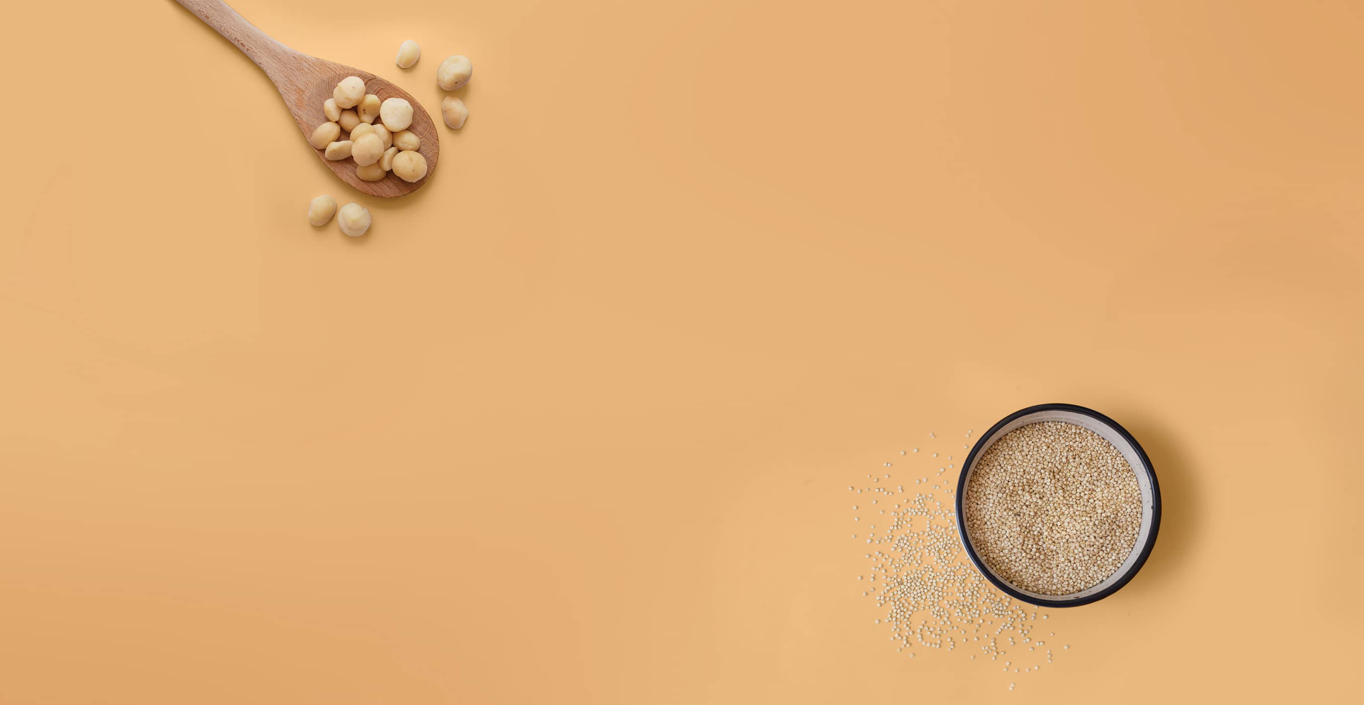 A spoonful of macadamia nuts and a dish of quinoa on a peach background