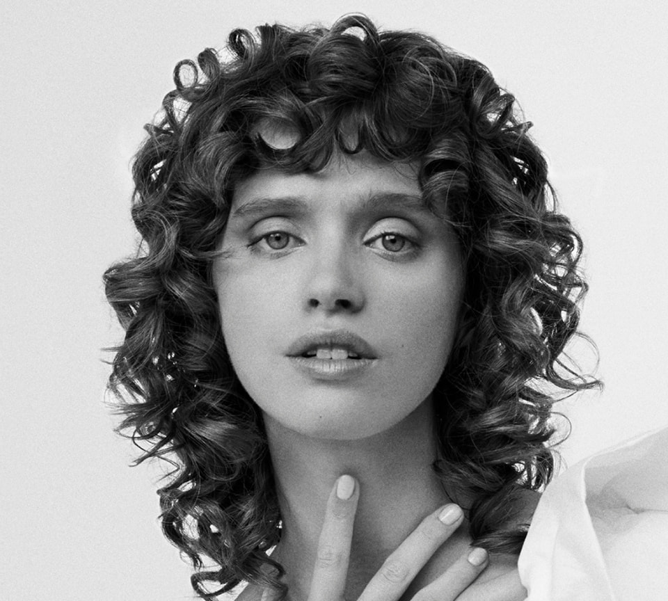 Black and white portrait of a woman with voluminous, tight curls and textured curly bangs.