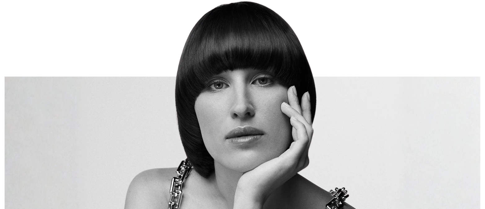 Monochrome portrait of a woman with a sleek bowl cut, resting her chin on her hand.
