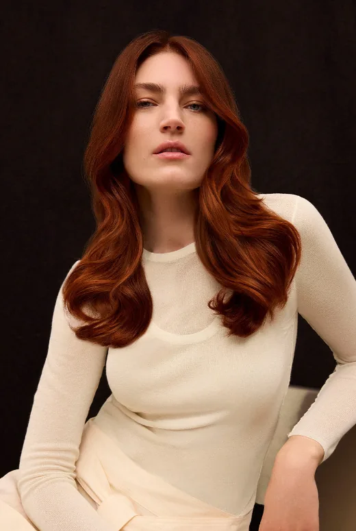 Model with long copper red hair, seated, in a cream top