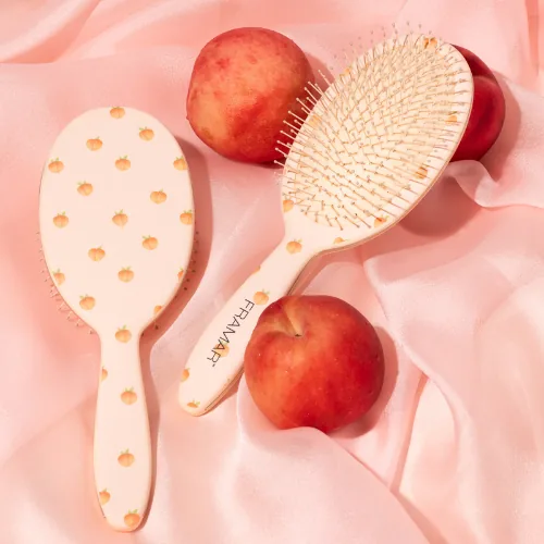 Two Framar Peach Please Georgia detangle brushes, cream with a peach print, among peaches