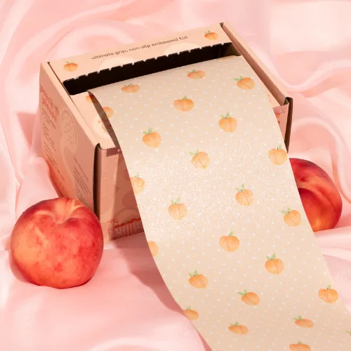 Framar Peach Please embossed foil, peach print, unrolling from its box across pink silk